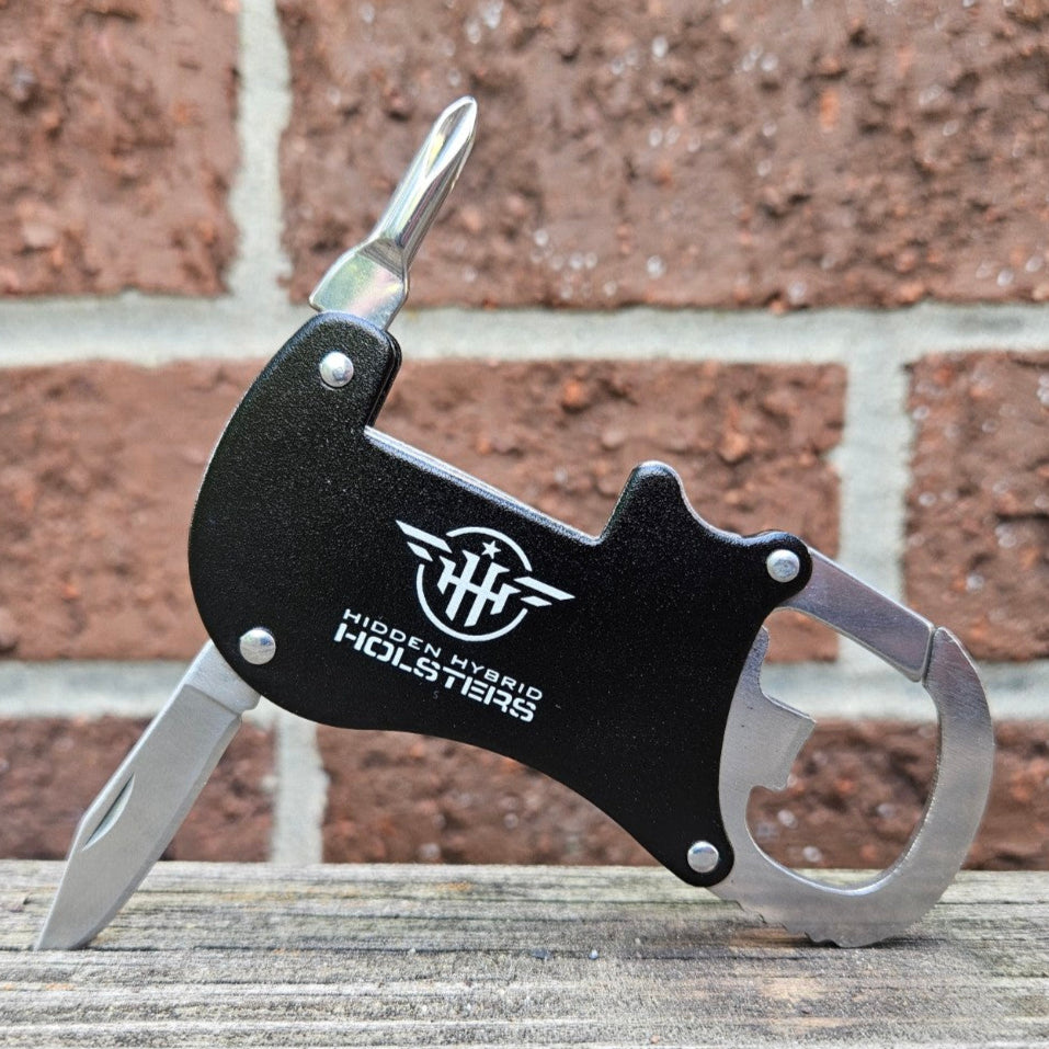 Metallic carabiner with bottle opener, philips screwdriver and letter opener on a wooden surface and brick wall background
