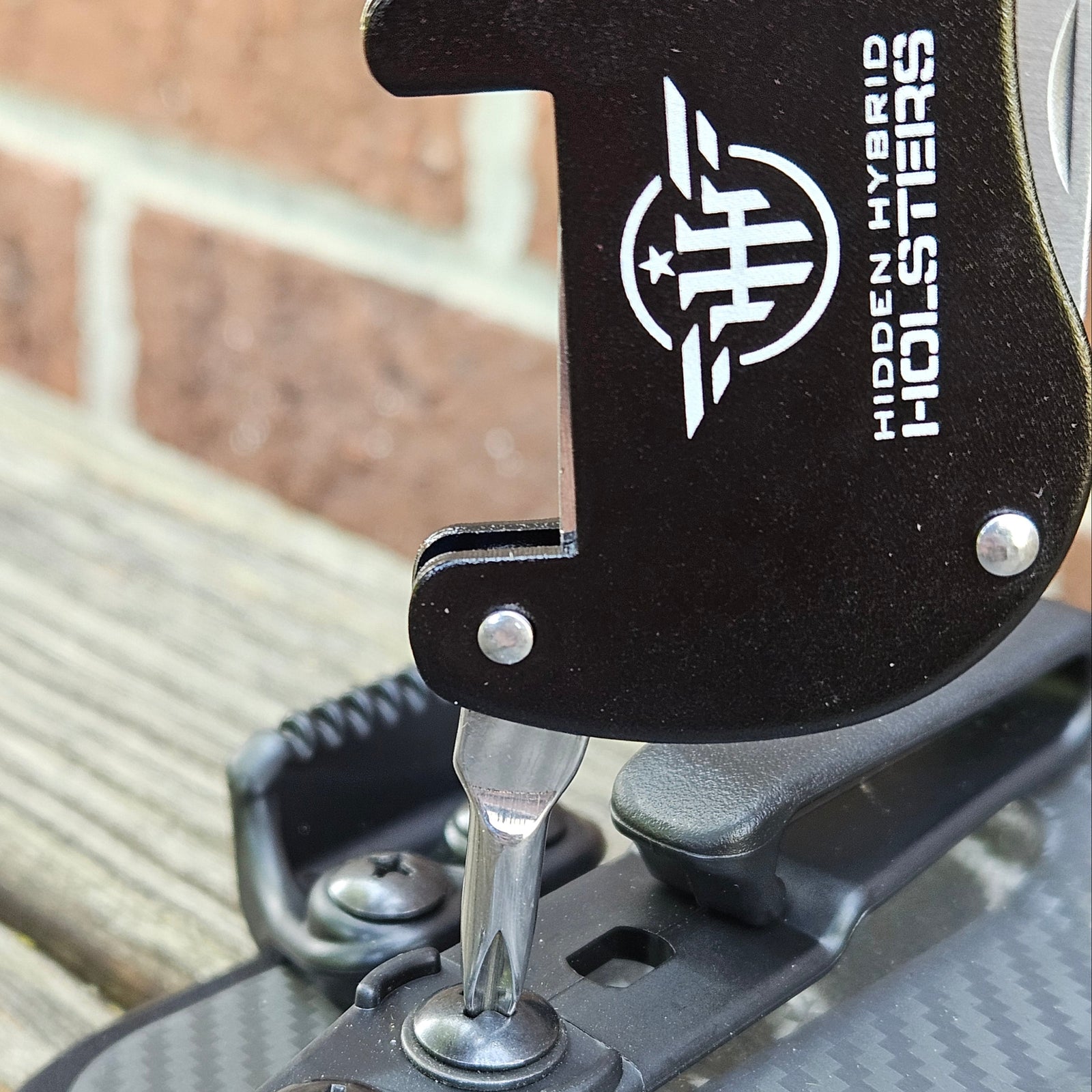 Metallic carabiner with bottle opener, philips screwdriver and letter opener on a wooden surface and brick wall background
